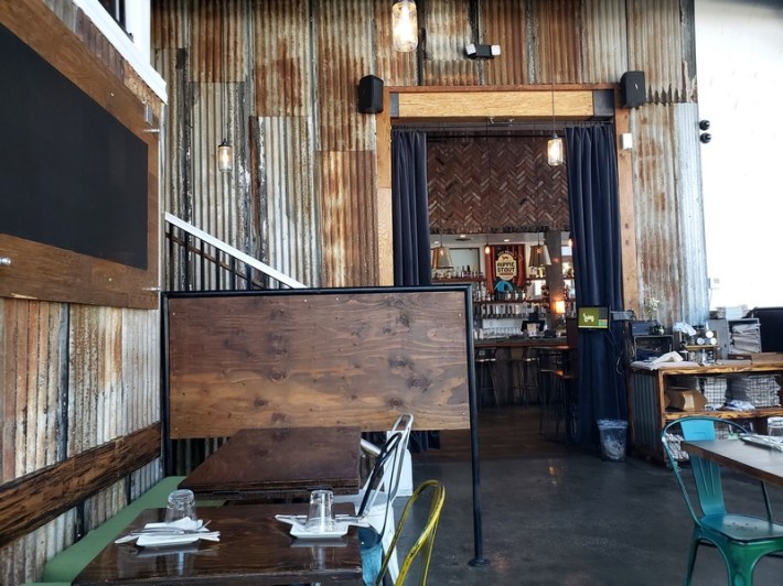 A look inside Sage Regenerative Kitchen in Echo Park, with a table, place settings, and a door leading into a bar framed by corrugated steel