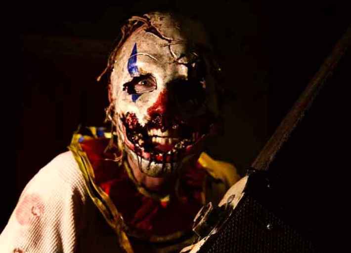 A clown with a ripped face and chainsaw