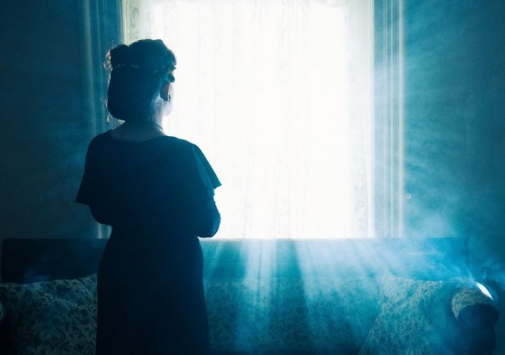 A woman stares at a ghostly light through a window