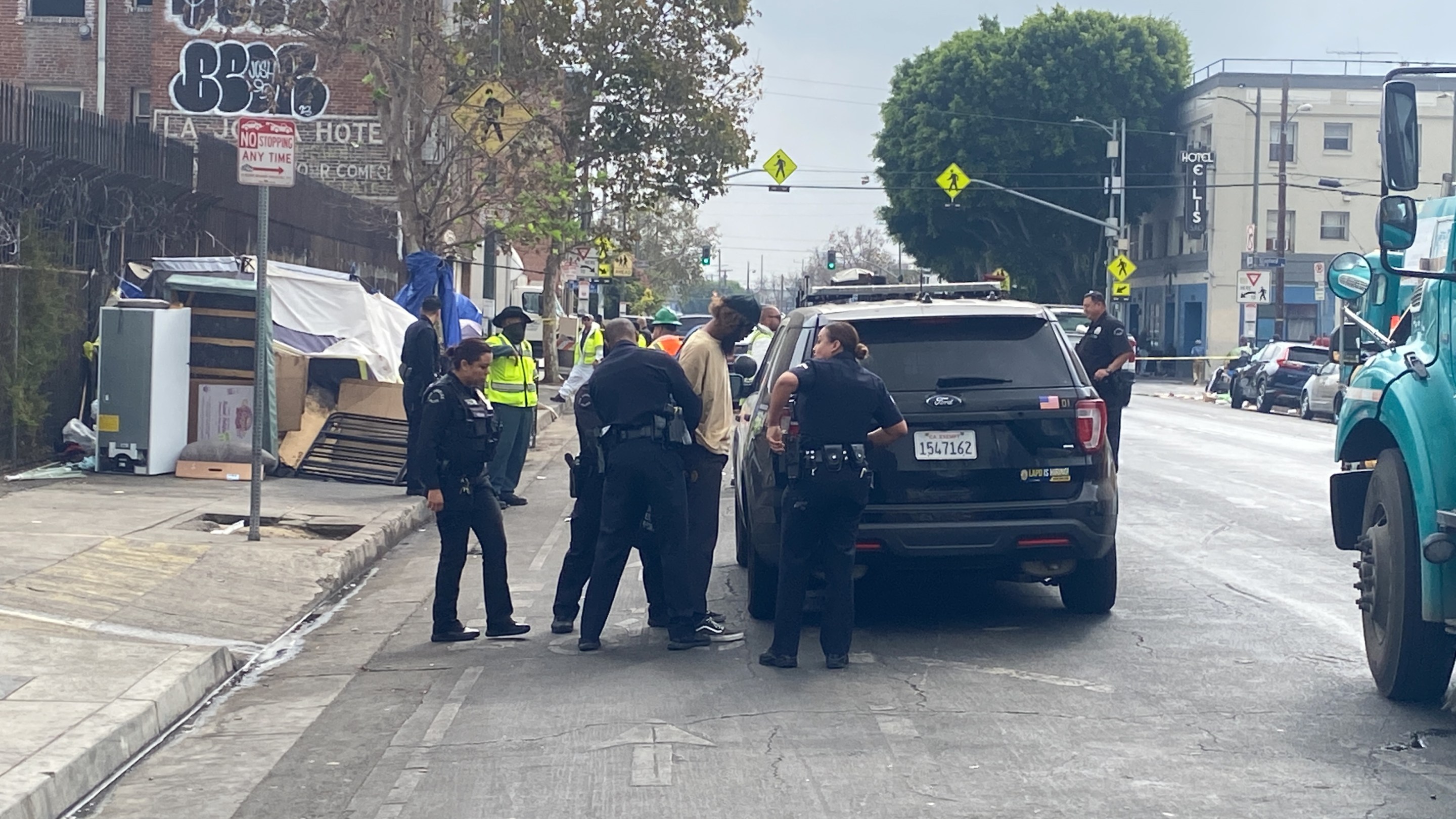 L.A. TACO Staff Investigative Reporter Lexis-Olivier Ray, is handcuffed while filming a sanitation "sweep." Officers are surrounding Ray and two officers are holding his arms and placing cuffs on him