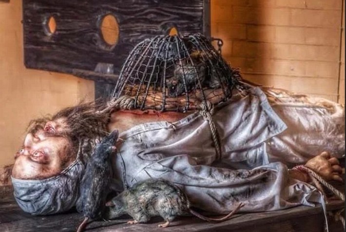 A man being tortured by rats trapped in a cage laid on his stomach